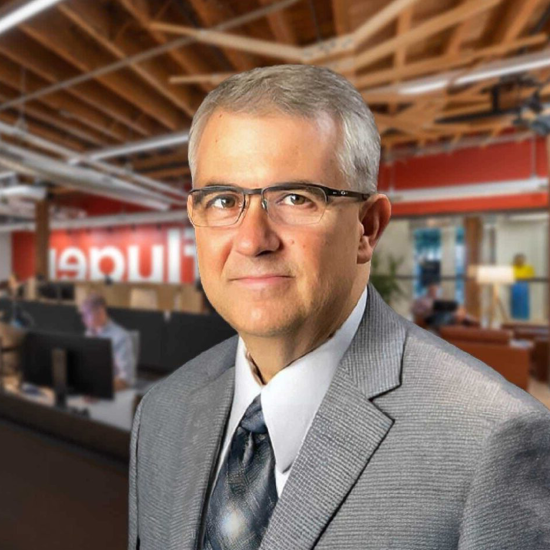 A man faces the viewer with an office background behind him.